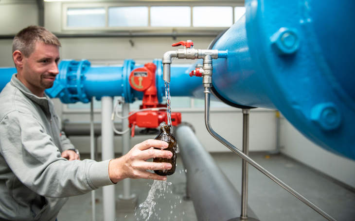 Mitarbeiter füllt Wasser in eine Flasche zur Qualitätskontrolle